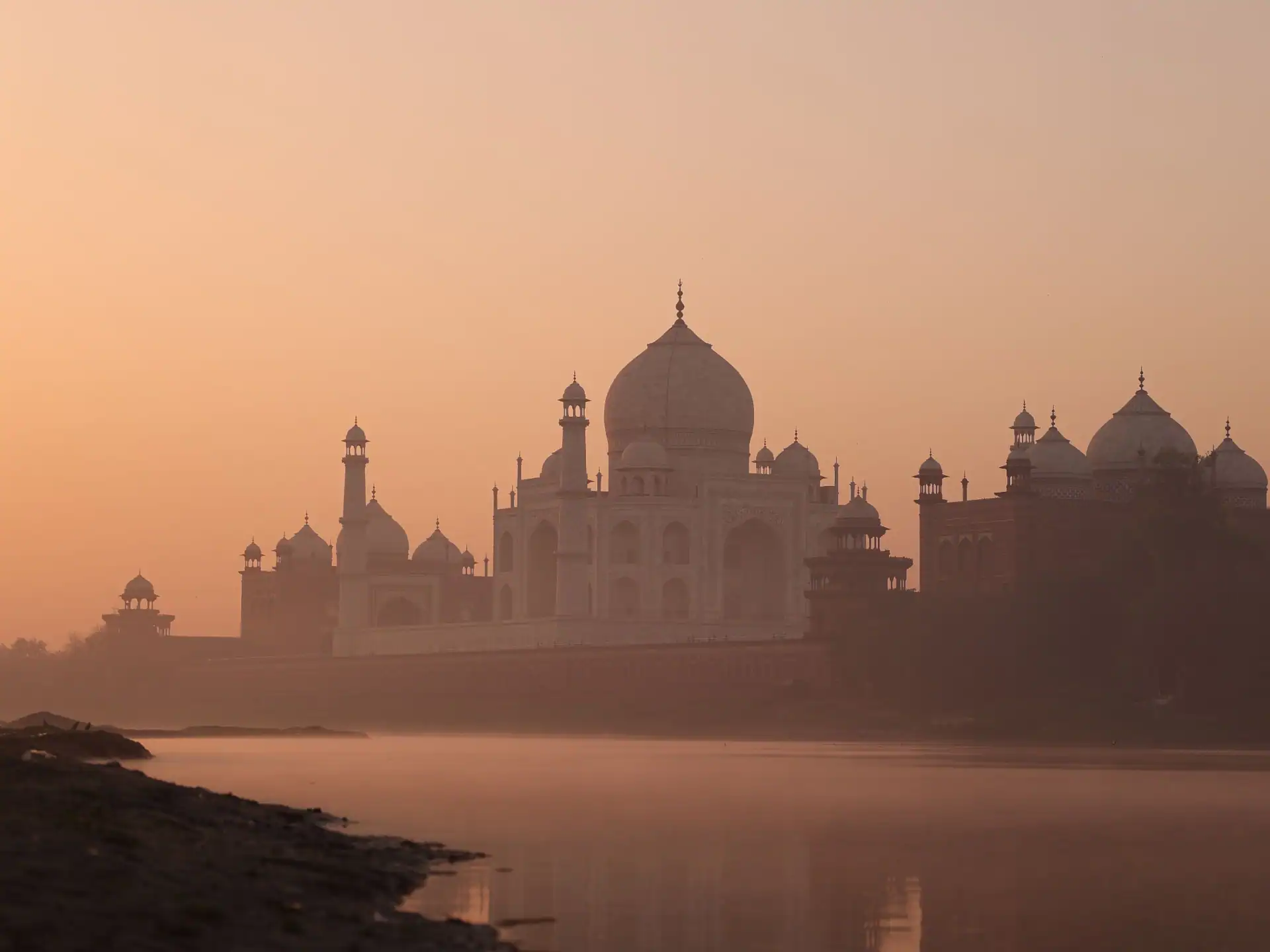 Taj Mahal seen from across the Yamuna river under a warm afternoon sky